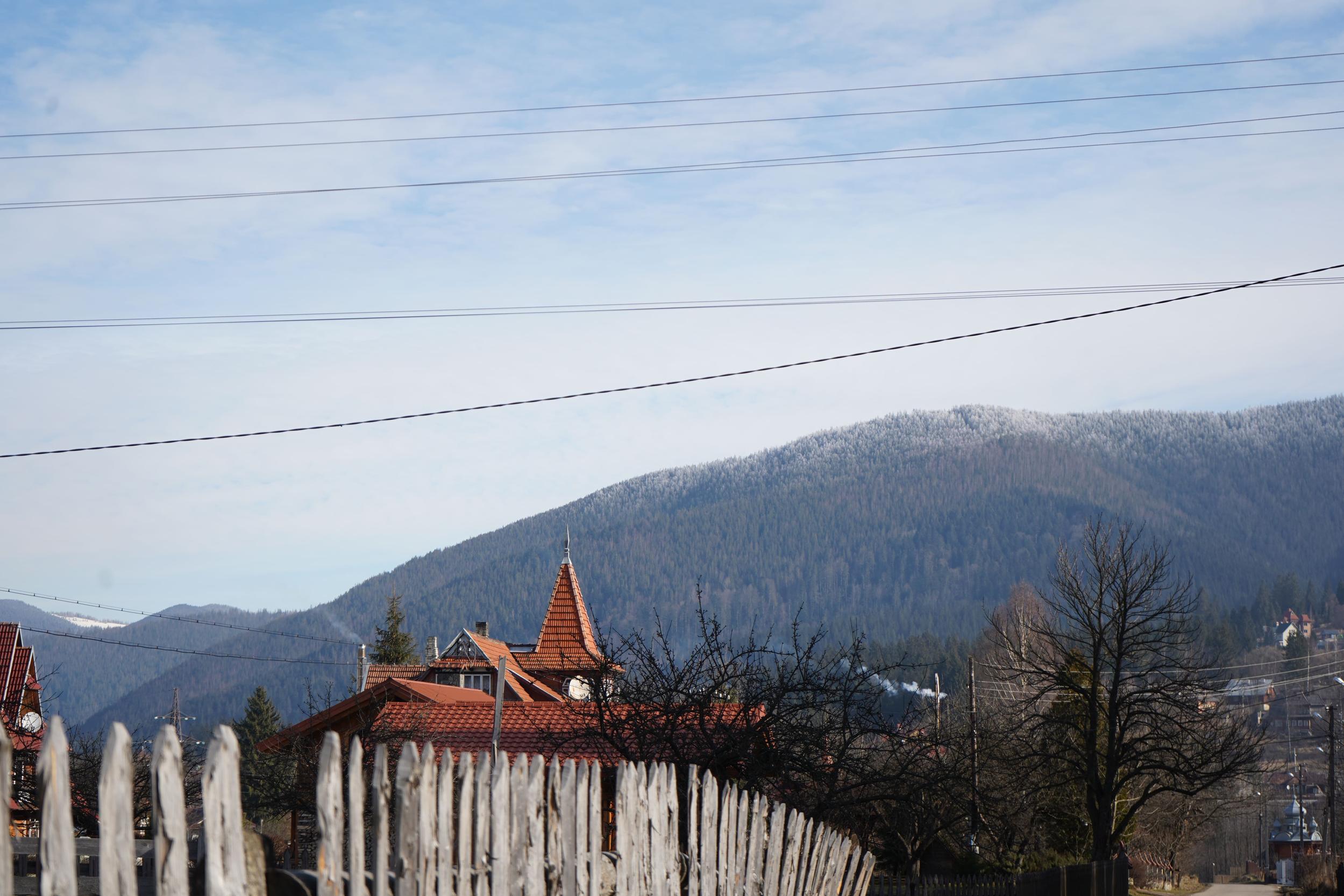 Malerischer Blick auf die ukrainischen Karpaten mit traditionellen Häusern und Holzzaun im Vordergrund.