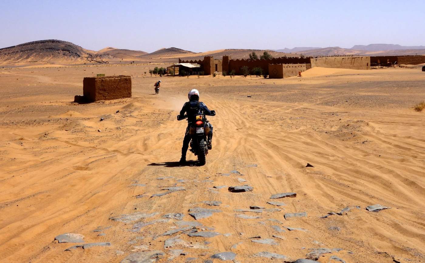 Enduro auf der Sandpiste bei einer Beduinenstätte im Erg Chebbi in Marokko